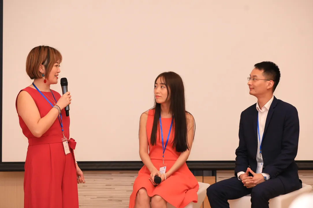 a woman holding a microphone talking to a man and a woman who are sitting down