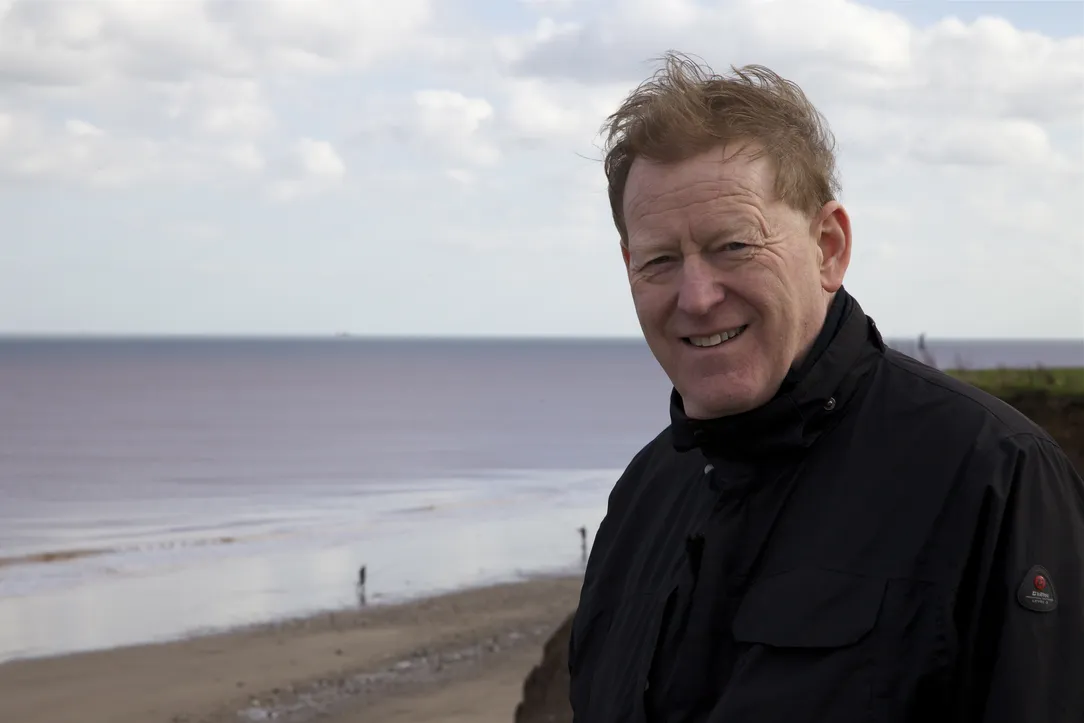 a man standing in a black jumper in front of the sea