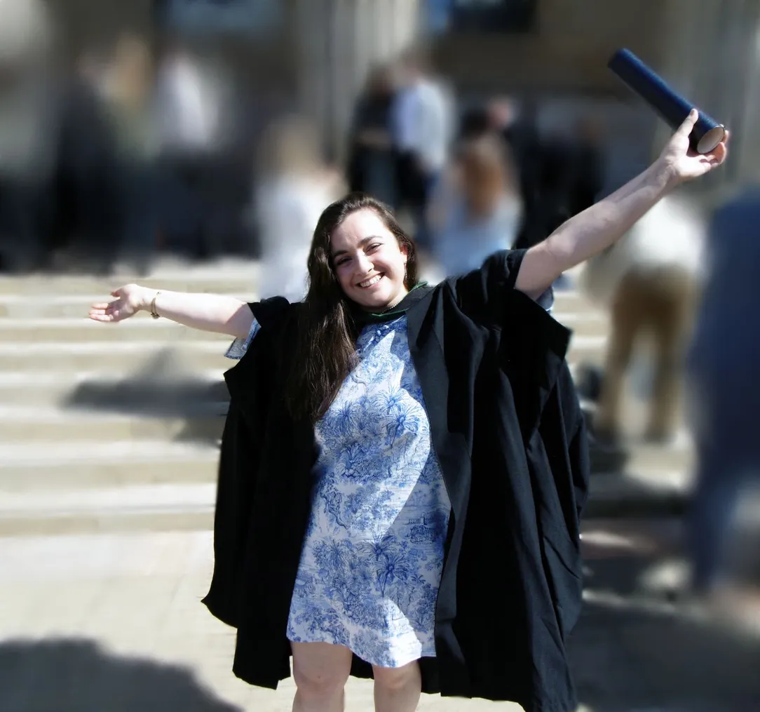 a student on graduation day with arms in the air and a certificate in her hand