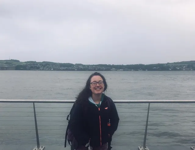 an image of claire standing in front of water with a railing behind her
