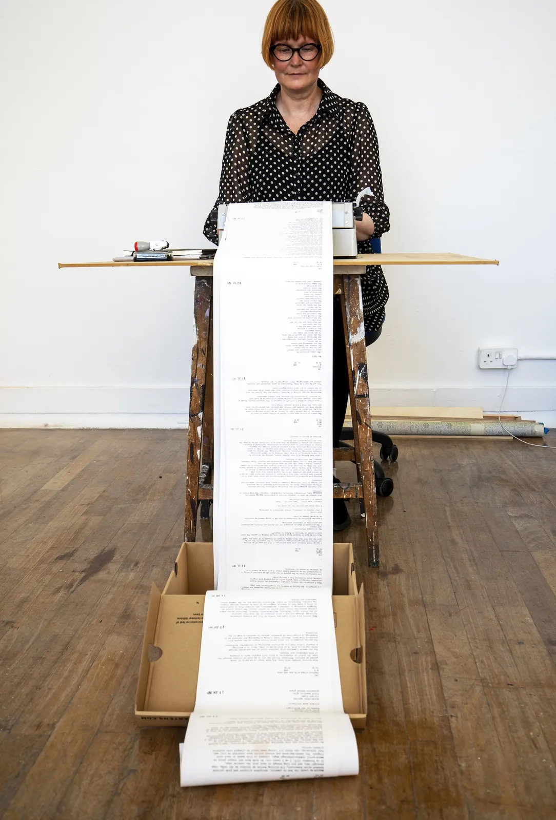 Mhairi Wild sitting at a table typing on an old type writer with a long paper rolling on the floor