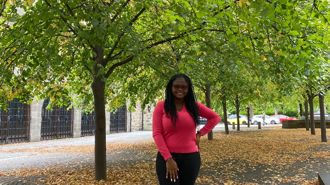 Dominica Araba Ansaba Ofori-Adjei standing under trees with lots of leaves on the ground