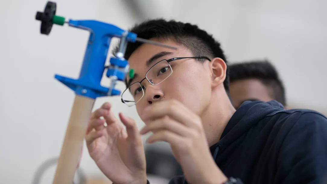 A student working with a wooden pole that has a blue metal structure on top as part of the windmill project 