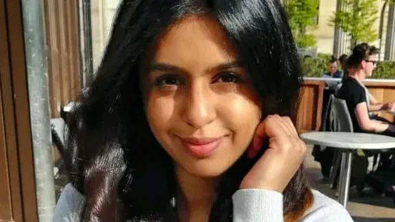 Roocha Kulkarni sits at a cafe with her hand by her face.