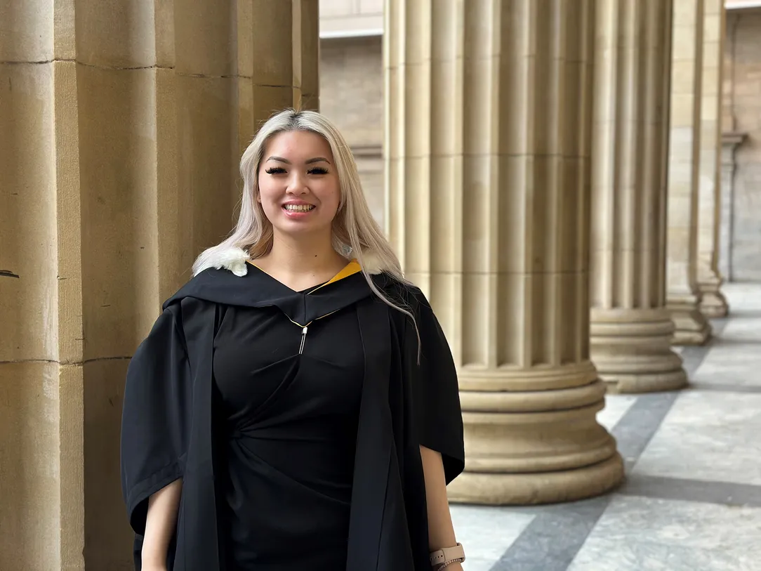 A graduate in a graduation gown outside of Caird Hall