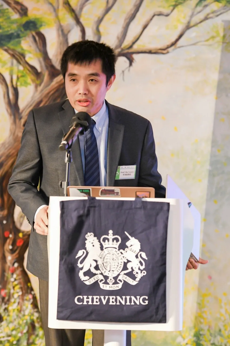 Prof Shawn Mu standing at a podium speaking at the forum. 
