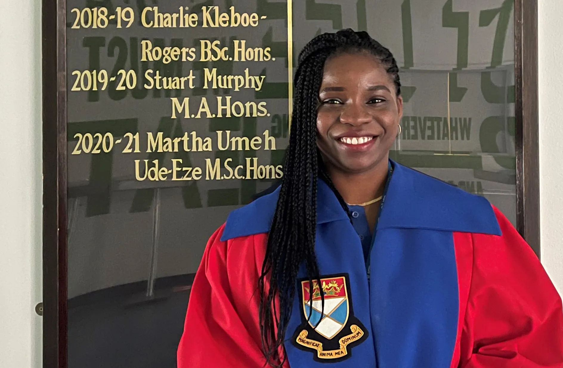 Martha Umeh Ude-Eze standing in front of her name on a board wearing a graduation gown