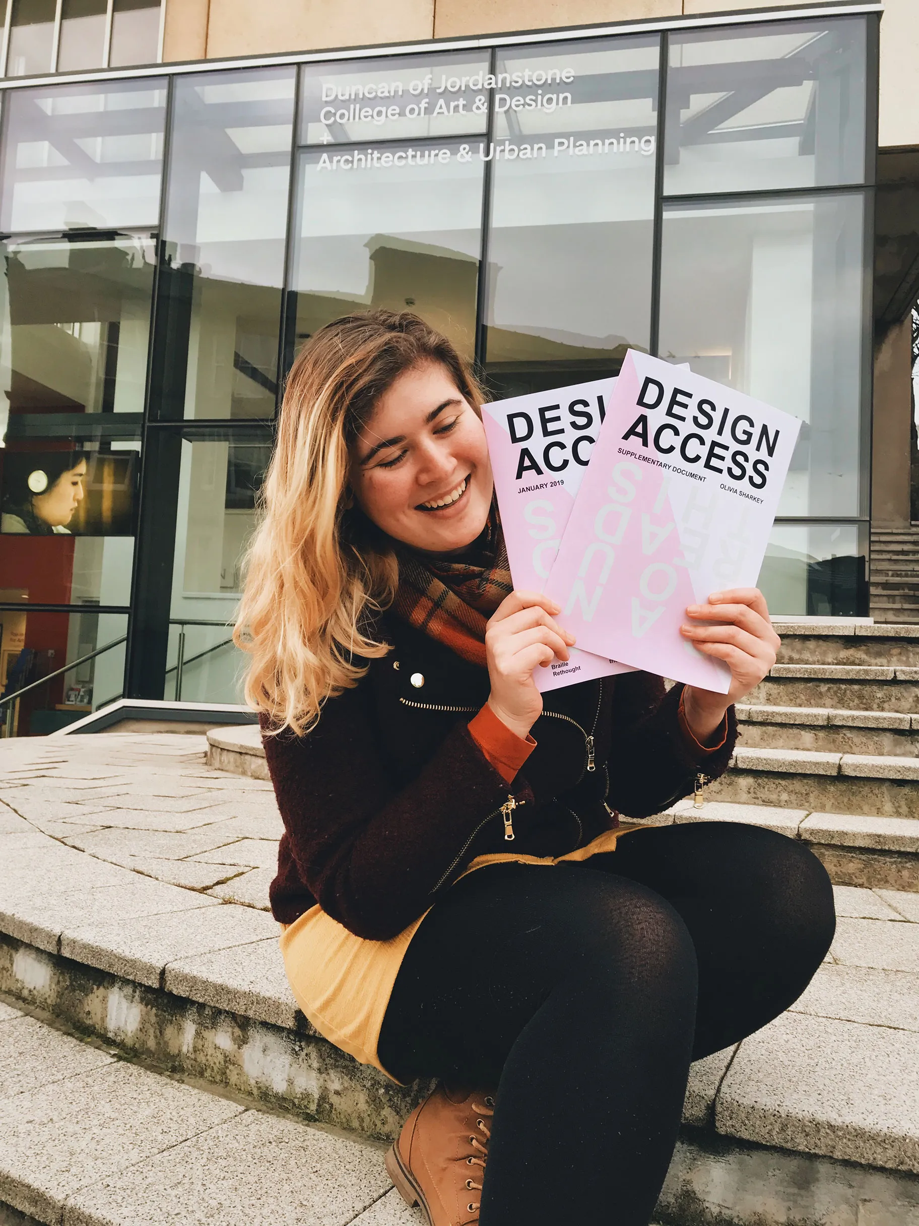 Olivia Sharkey sitting in front of DJCAD with her brochures Design Access