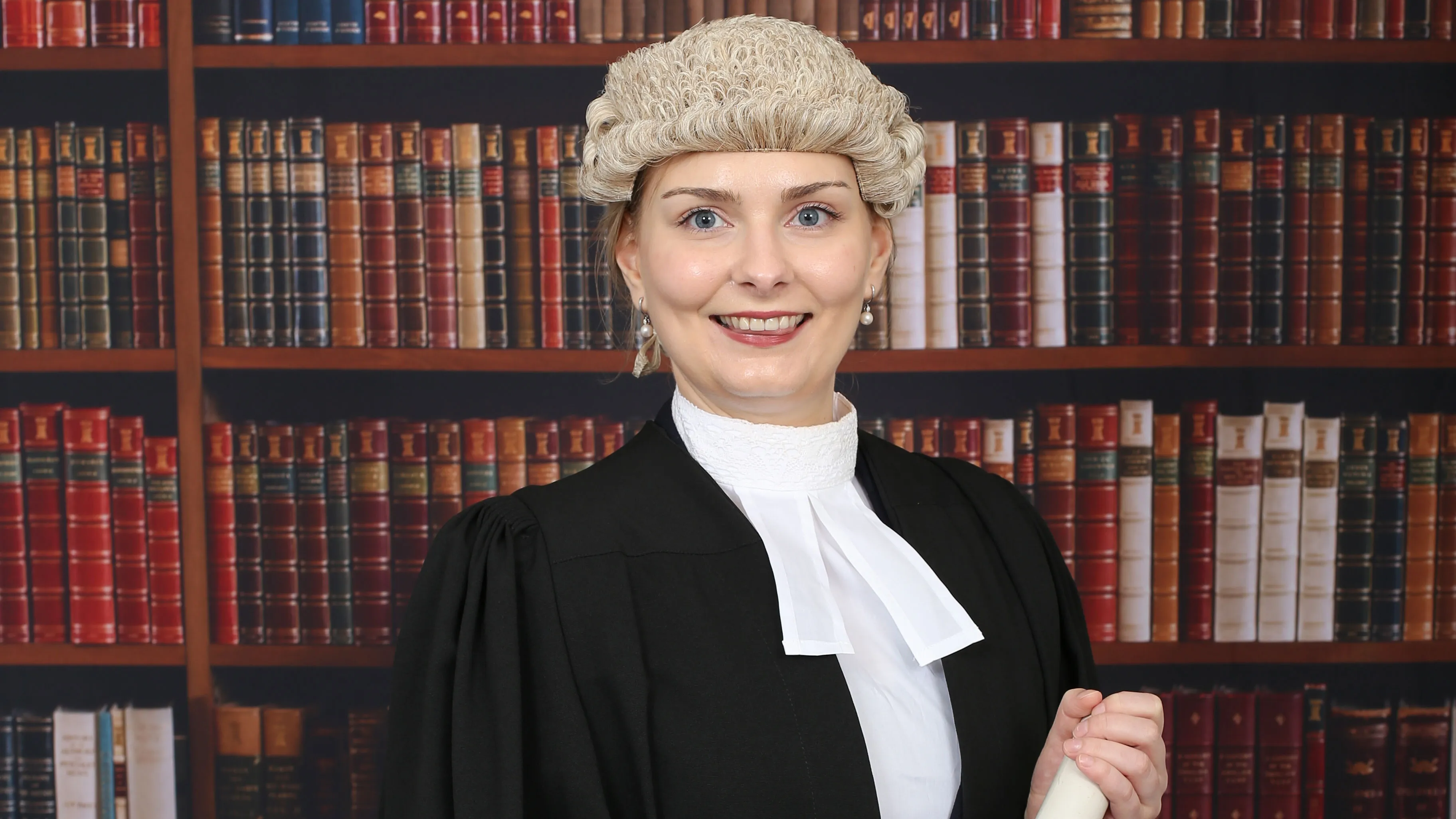 Kathleen Sargent wearing robes and Tie Wig, standing in front of shelf of books