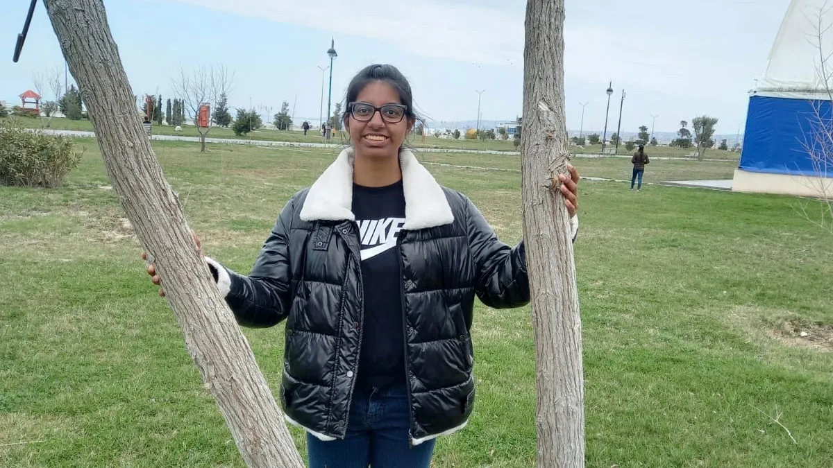 Akanksha Joshi standing on the grass between two branches of a tree.