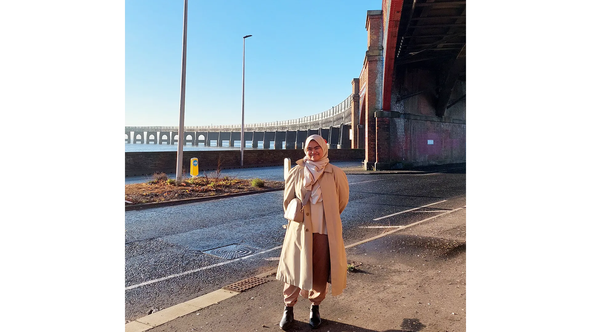 Azizah Azis standing under the Tay Rail Bridge with the River Tay behind her