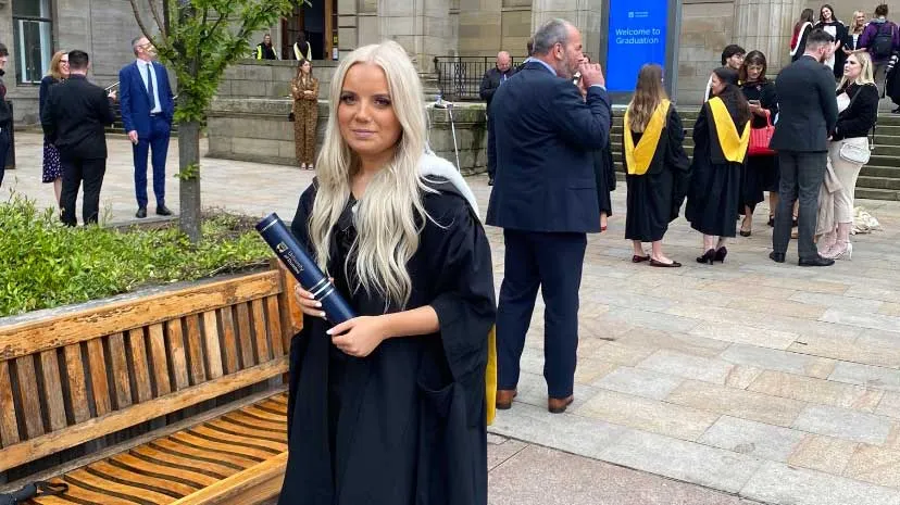 Alisha Innes wearing graduation robes and holding her degree.