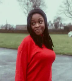 A girl in a red top looks over her right shoulder.