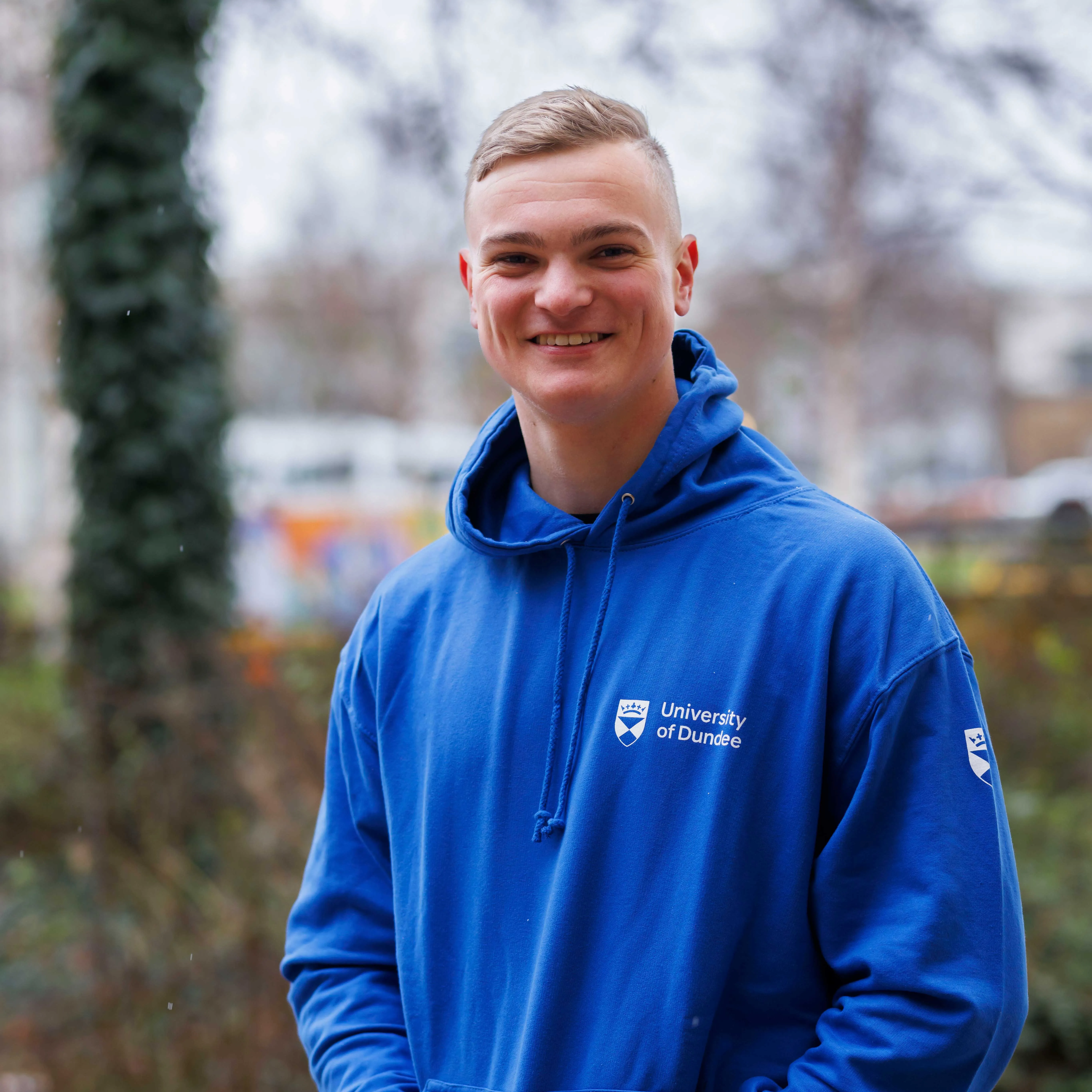 Bradley Schreiber wearing a blue UoD hoody, standing outside.