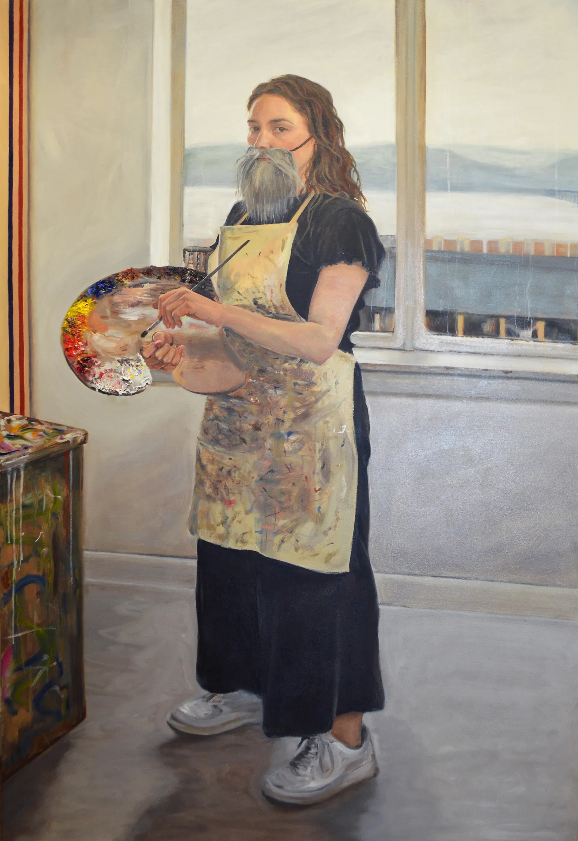 A painter in a studio holds a palette and brush, wearing an apron and a fake gray beard, standing by a window with a scenic view