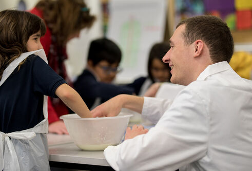 A teacher helping a girl mixing something in a bowl
