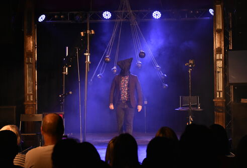Kevin Quantum standing under blue smoke stage lights with a sack on his head