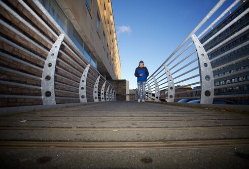 a student walking towards the camera across a bridge