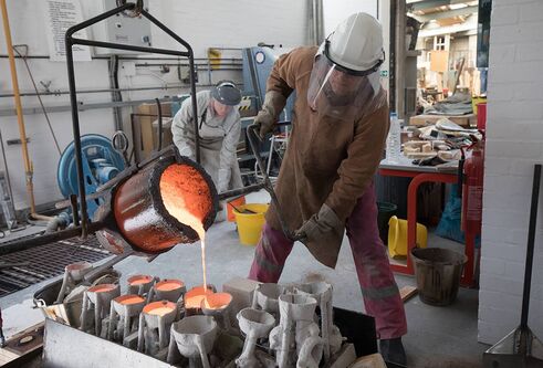 a person in protective gear pouring molten metal into moulds