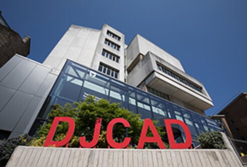 DJCAD exterior with a large red sign outside a glass-fronted concrete building under a blue sky
