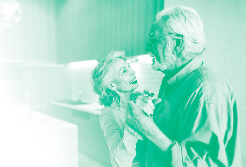 An elderly couple dance in their kitchen with a green colour wash over the photo