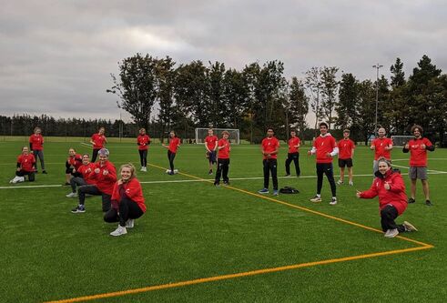 group of students in red sports attire on green grass pitch 