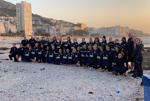 the Scottish womens rugby team posing for a photograph with snow on the ground and some buildings behind them