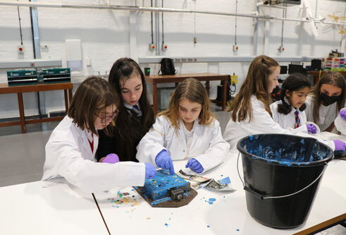 three young primary school aged girls standing at white desk, sorting blue concrete mix into moulds 