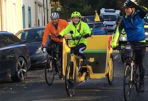 two men riding bikes following a young girl in hi-vis gear riding a rickshaw