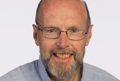 head shot of man wearing light blue shirt and thin glasses