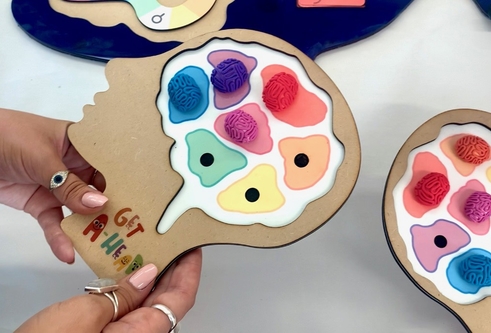 hands holding a head shaped piece of wood, that has the outline of a brain with colourful, miniature pieces of brains stuck on top