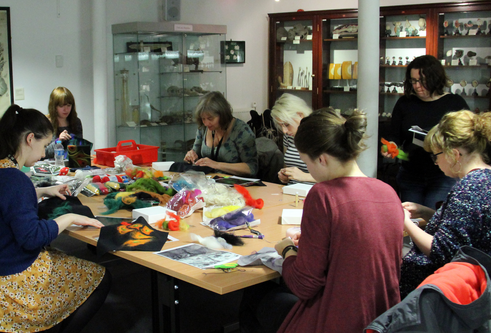 group of people sitting down at a table doing some needle felting crafts