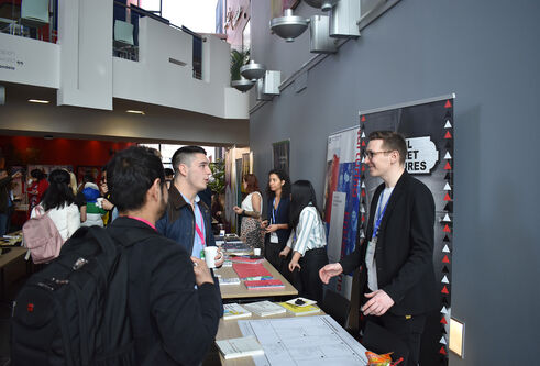 People standing in the Dalhousie Building foyer visiting tables with books and posters for the Venture 2021 competition