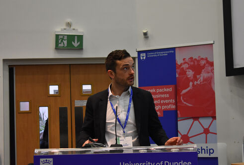 Brian McNicoll standing at a podium with Centre for Entrepreneurship banner at the front presenting at the Venture competition for 2022