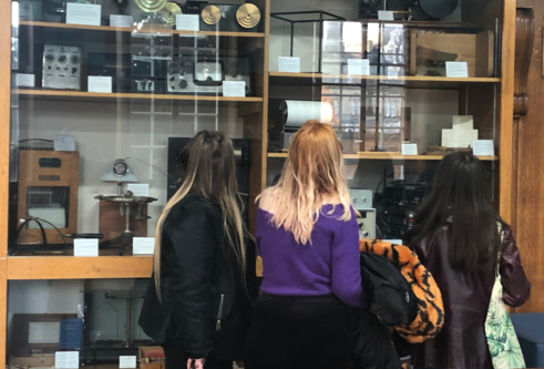 three students with their backs turned stand looking at a display case full of psychology testing equipment