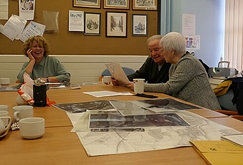 A female archivist and two older community members sit at a table discussing large photograph images of Dundee