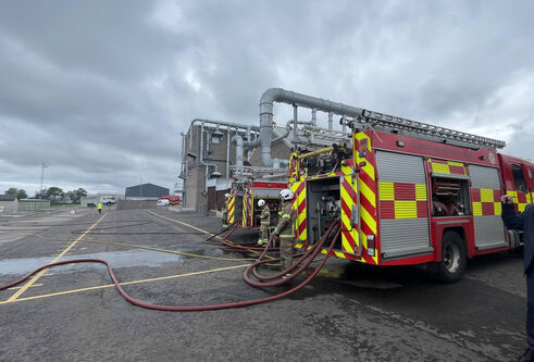 The back of two fire trucjs with water houses leading out and off of the image