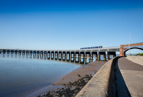 Train crossing bridge over River Tay against bright blue sky