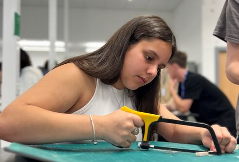 a female secondary school pupil sawing a small piece of wood at the EMBEDD programme