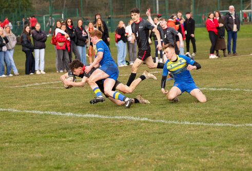 action shot of people playing rugby outside on grass with spectators in background