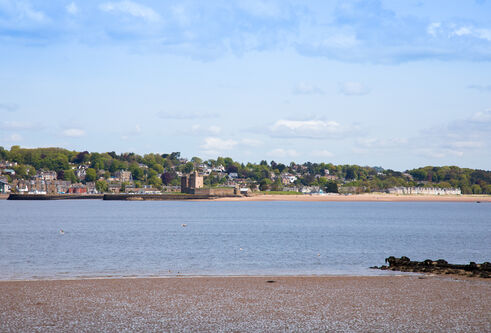Sandy beach looking out towards sea, over to another sandy beach and town built onto a hill.