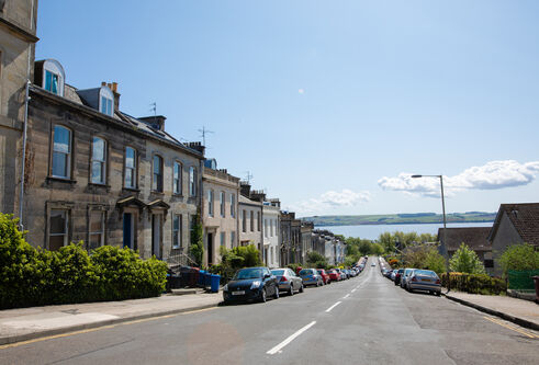 Street with older style buildings and cars parked along the kerb, road leading down to sea at end of street