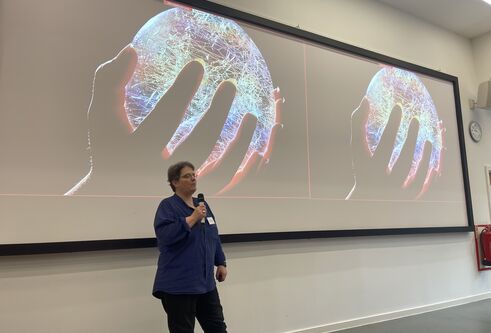 Image of Professor Niamh Nic Daeid presenting in front of an image of a hand holding a round sphere representing a globe which is lit up and full of electronics