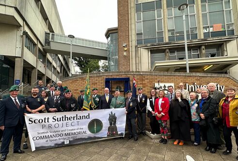 A group of people, some i nkilts and formal wear, holding up a large sign
