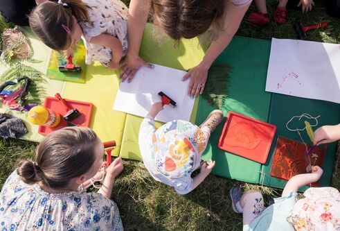 View from above of  young children sitting on grass and painting with their carers