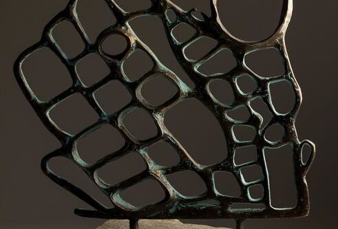 Sculptural metal piece with holes and spikes on a stone pedestal.