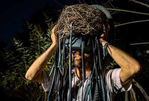 Man with a VR head set with blue fabric and twigs hanging from his head