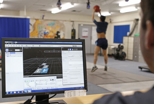 A close shot of a man looking at a computer monitor. Blurred in the background, a man jumps with a ball