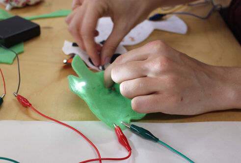 Two hands hold a piece of green material with electric wires clipped to it.