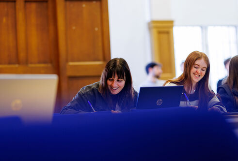 A couple of students sitting side by side taking notes 